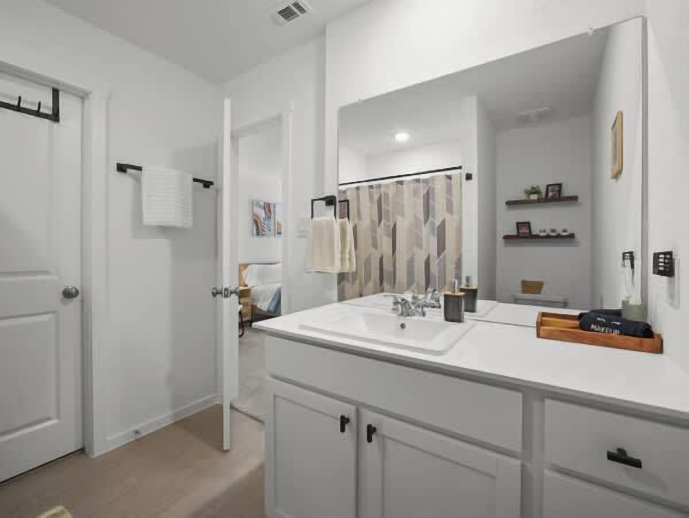 A modern bathroom with a large mirror, white cabinetry, and a shower curtain with a geometric pattern.