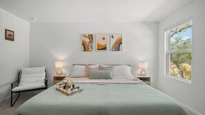 Een slaapkamer met een bed, nachtkastjes, een stoel en kunst aan de muur.