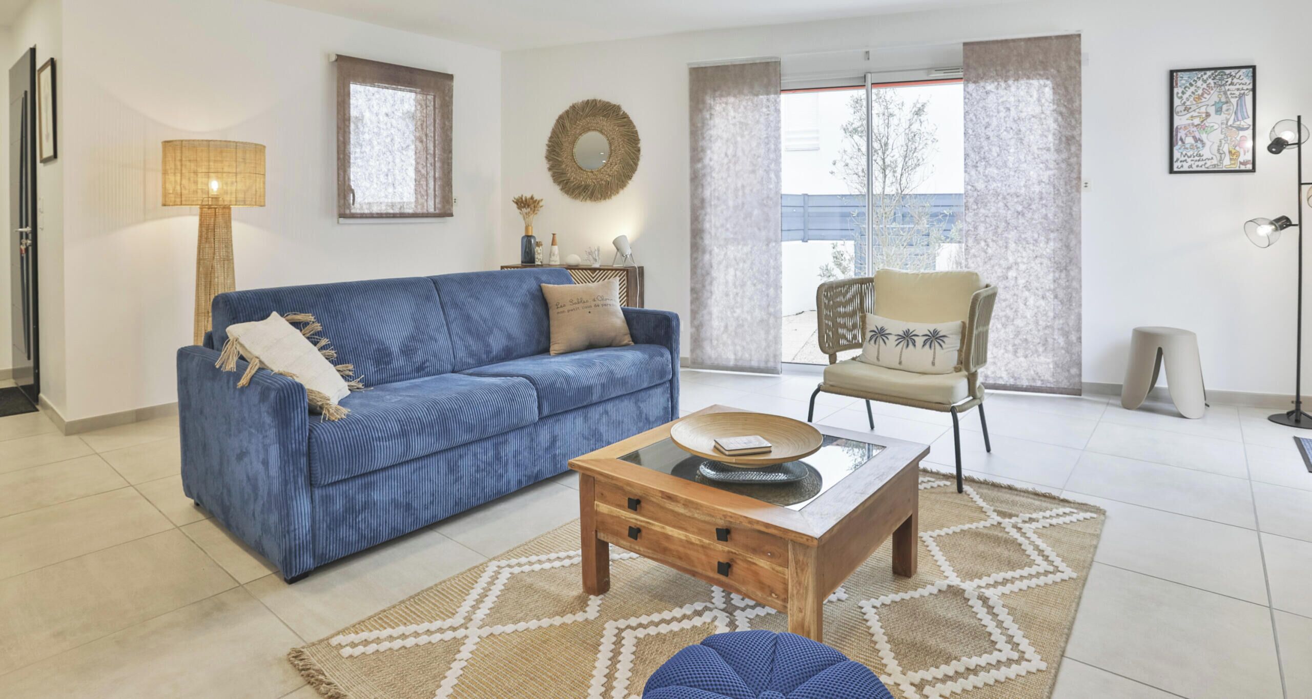 Un salon avec un canapé bleu, une table basse en bois, un tapis à motifs et un fauteuil avec un coussin.