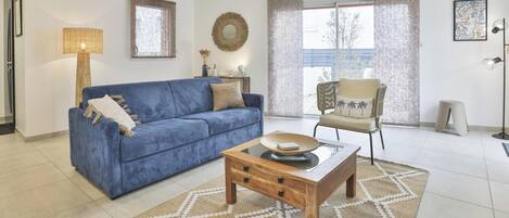 Un salon avec un canapé bleu, une table basse en bois, un tapis à motifs et un fauteuil avec un coussin.