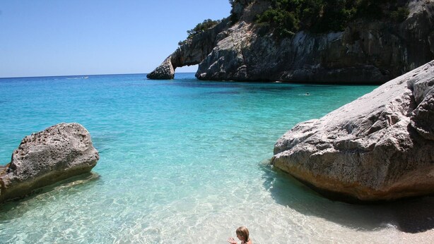 A beach with clear turquoise water, large rocks, and a child playing in the shallow water. - Detached cottage with spaiggia within walking distance, sea d mountain view! (Santa Maria Navarrese)