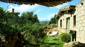 A stone building with a garden area, including a lawn, a white lounge chair, and potted plants. - Detached cottage with spaiggia within walking distance, sea d mountain view! (Santa Maria Navarrese)