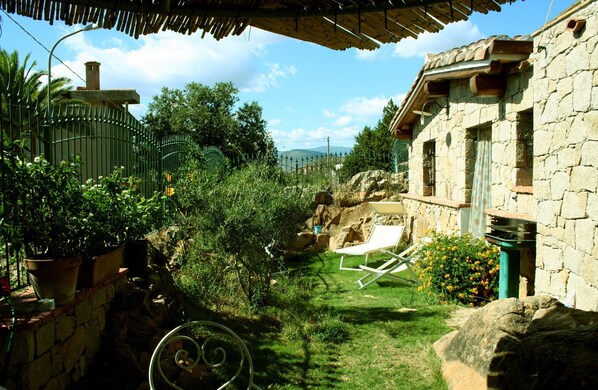 A stone building with a garden area, including a lawn, a white lounge chair, and potted plants.