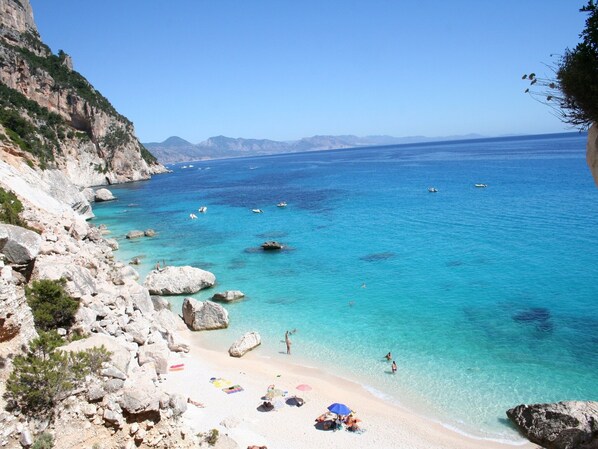 Ein Küstenstrand mit klarem türkisblauem Wasser, felsigen Klippen und einem Sandstrand.