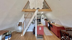 A loft-style apartment with a wooden staircase, a kitchen with red cabinets, and a dining area with a wooden table and chairs. - Serene 2-bedroom A-Frame in Jefferson perfect for Hot Tub + Views + Stargazing (Jefferson)