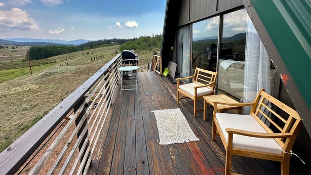A wooden deck with a glass balustrade overlooking a grassy landscape. - Serene 2-bedroom A-Frame in Jefferson perfect for Hot Tub + Views + Stargazing (Jefferson)