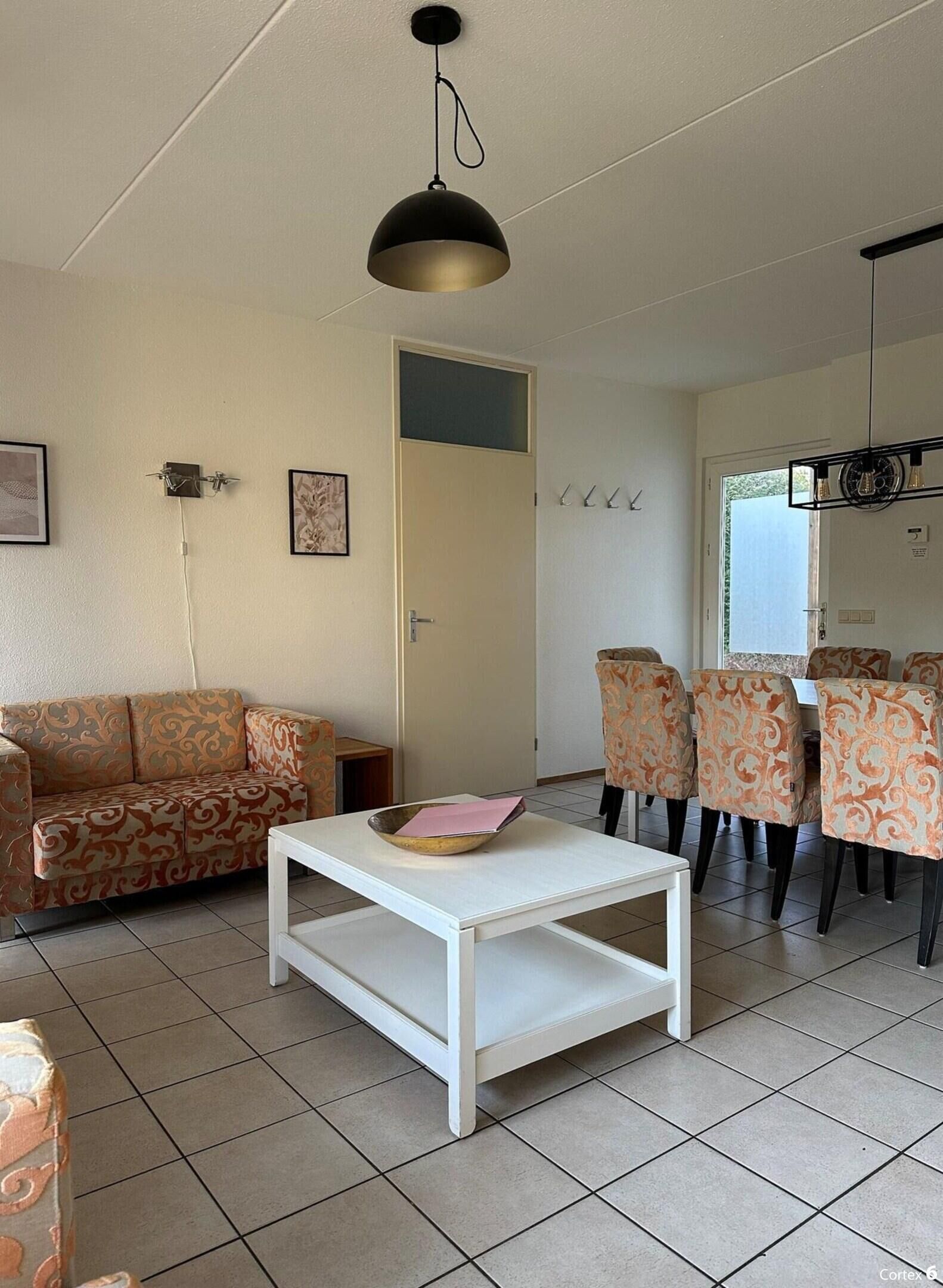A living room with a sofa, a coffee table, patterned chairs, a dining table, and a hanging light fixture.