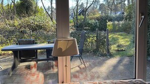 A room with a large sliding glass door leading to a garden. Inside, there is a patterned sofa and a table with chairs. - Spacious Ground-floor Apartment in Lochem (Lochem)