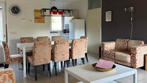 A modern living room with a dining area, patterned chairs, a white coffee table, and a black pendant light. - Spacious Ground-floor Apartment in Lochem (Lochem)