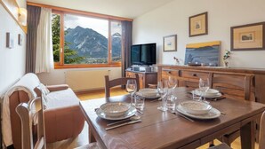 Un coin repas avec vue sur la montagne, une télévision et une table à manger dressée avec des assiettes et des verres.