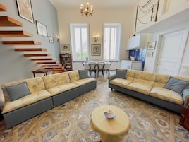 Una sala de estar con dos sofás, una mesa de centro y una escalera. Se observa un comedor con una mesa y sillas al fondo.