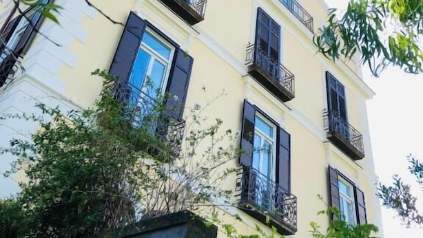Un edificio de varios pisos con balcones y ventanas, rodeado de vegetación.