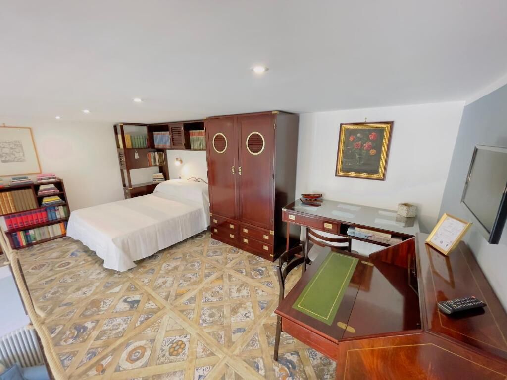 A compact hotel room with a bed, a desk, a chair, a bookshelf, and a television.