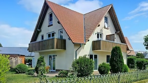 Ein zweistöckiges Haus mit geneigtem Dach, Balkonen und einem umzäunten Garten.