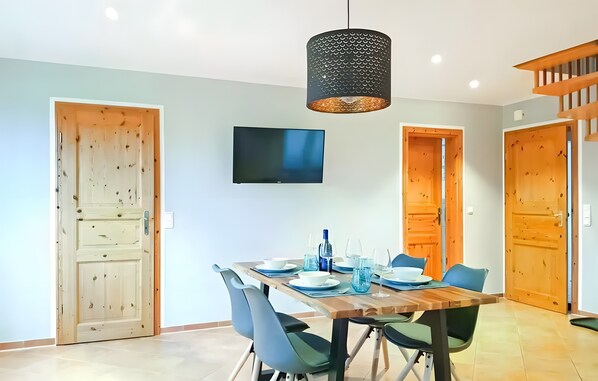 A dining area with a wooden table, chairs, a TV, and a hanging light fixture. - Holiday Home Rechlin See Apartment 1 (Rechlin)