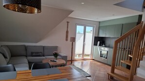 Um espaço de estar moderno com área de jantar, sofá, mesa de centro e cozinha, com escada de madeira.