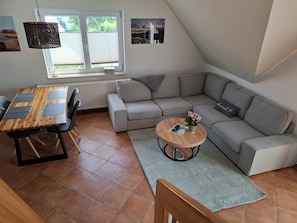 A cozy living area with a wooden dining table, grey sofa, and a small coffee table with a book and flowers. - Holiday Home Rechlin Lake Apartment 2 (Rechlin)