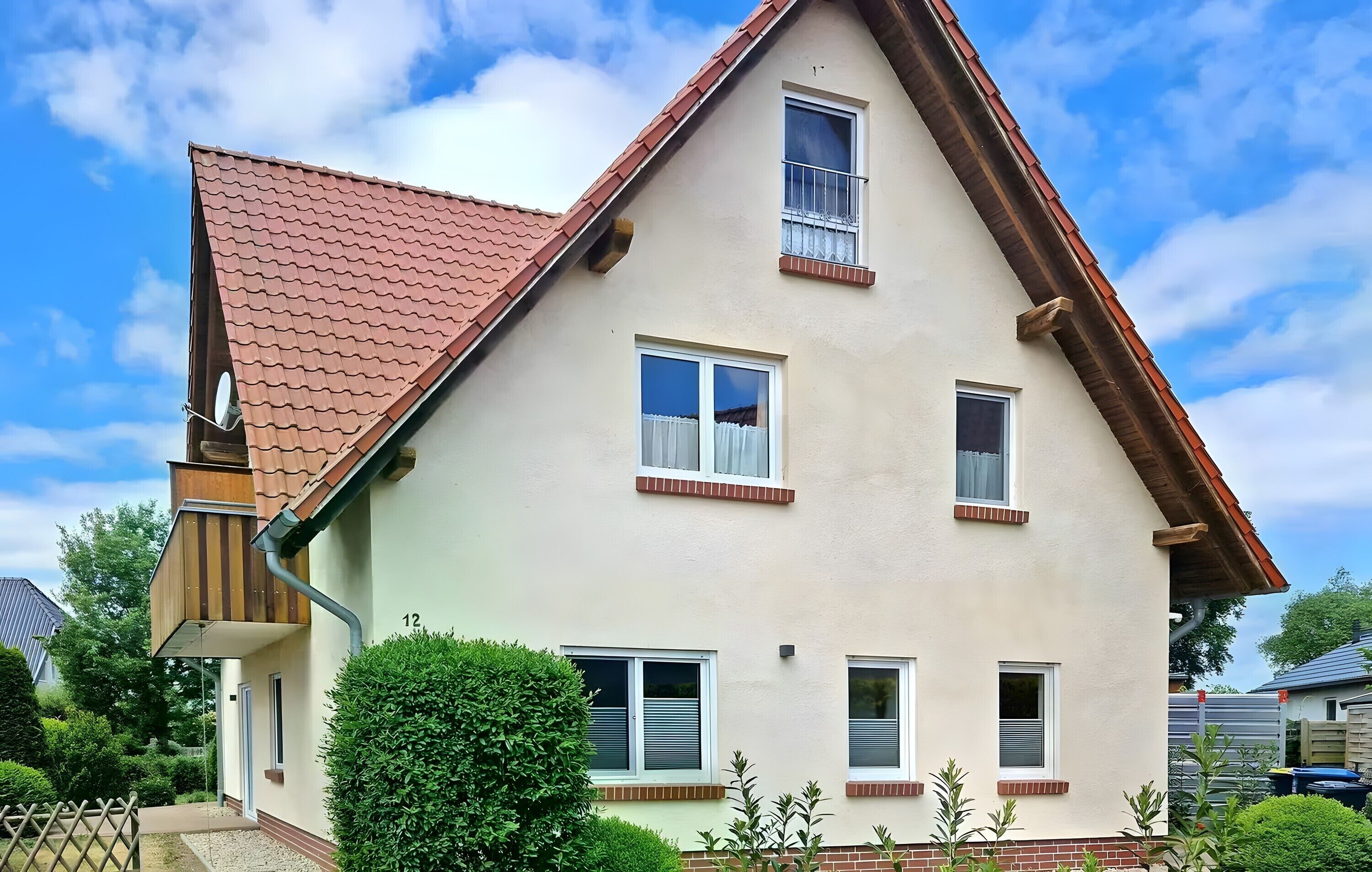 A two-story house with a red-tiled roof, multiple windows, and a small balcony.