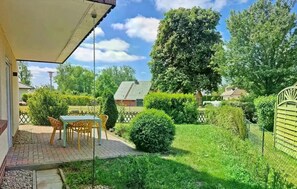 A patio with a table and chairs, surrounded by well-maintained hedges and a large tree. - Holiday Home Rechlin Lake Apartment 3 (Rechlin)