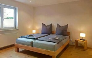 Ein Doppelbett mit Holzbettrahmen, zwei Nachttische mit Lampen und ein Fenster mit Jalousien.