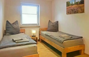 A small, cozy room with two single beds, a window, a radiator, and a small table. - Holiday Home Rechlin Lake Apartment 3 (Rechlin)