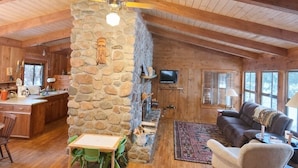 A spacious living area with a stone fireplace, wooden ceiling beams, a dining table with chairs, and a cozy seating area with a sofa and armchairs. - The Hidey-Ho on Lower Clam Lake | Secluded | Private Dock (Clam Lake)