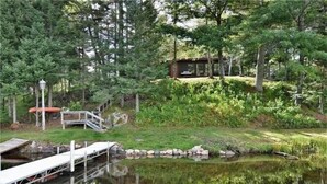 A cabin surrounded by dense forest, a dock extending into a calm lake, and a small staircase leading to the cabin. - The Hidey-Ho on Lower Clam Lake | Secluded | Private Dock (Clam Lake)