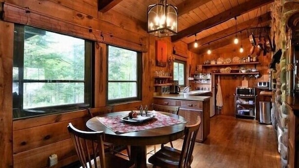 A wooden cabin interior with a dining area, kitchen, and large windows. - The Hidey-Ho on Lower Clam Lake | Secluded | Private Dock (Clam Lake)