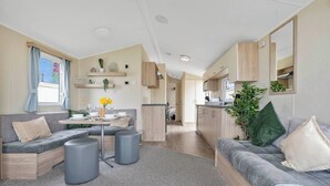A compact living space with a sofa, ottoman, and a dining table. There is a kitchen area with cabinets and a countertop. - Cozy Coastal Retreat 3-bedroom Lodge at (Prestonpans)