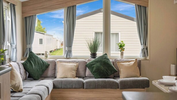 A cozy living room with a large sectional sofa, a dining table, and a view of a white house through large windows. - Cozy Coastal Retreat 3-bedroom Lodge at (Prestonpans)