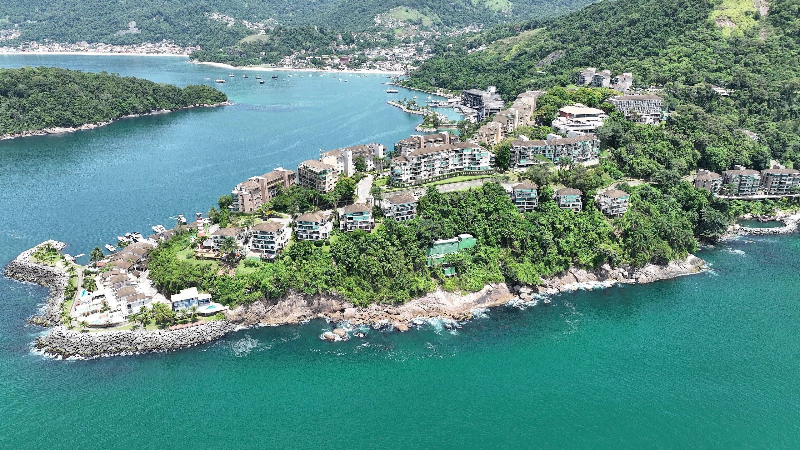 An aerial view of a coastal resort with multiple buildings, a rocky shoreline, and a bay with boats.