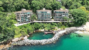 A multi-story hotel with balconies, located near a rocky shoreline and surrounded by dense greenery. - Porto Real Resort - Daily Rates and Seasonal Rates (Mangaratiba)