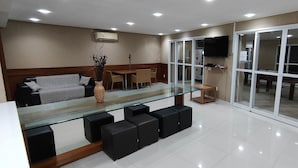 A modern kitchen with a glass counter, black stools, a dining area with chairs, and a TV mounted on the wall. - Porto Real Resort - Daily Rates and Seasonal Rates (Mangaratiba)