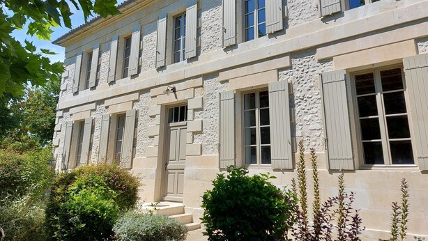 Un edificio a più piani con facciata in pietra, numerose finestre con persiane e un ingresso centrale con gradini.