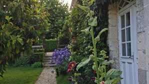 Un vialetto fiorito conduce a un edificio con una porta e una finestra bianca, immerso nel verde.
