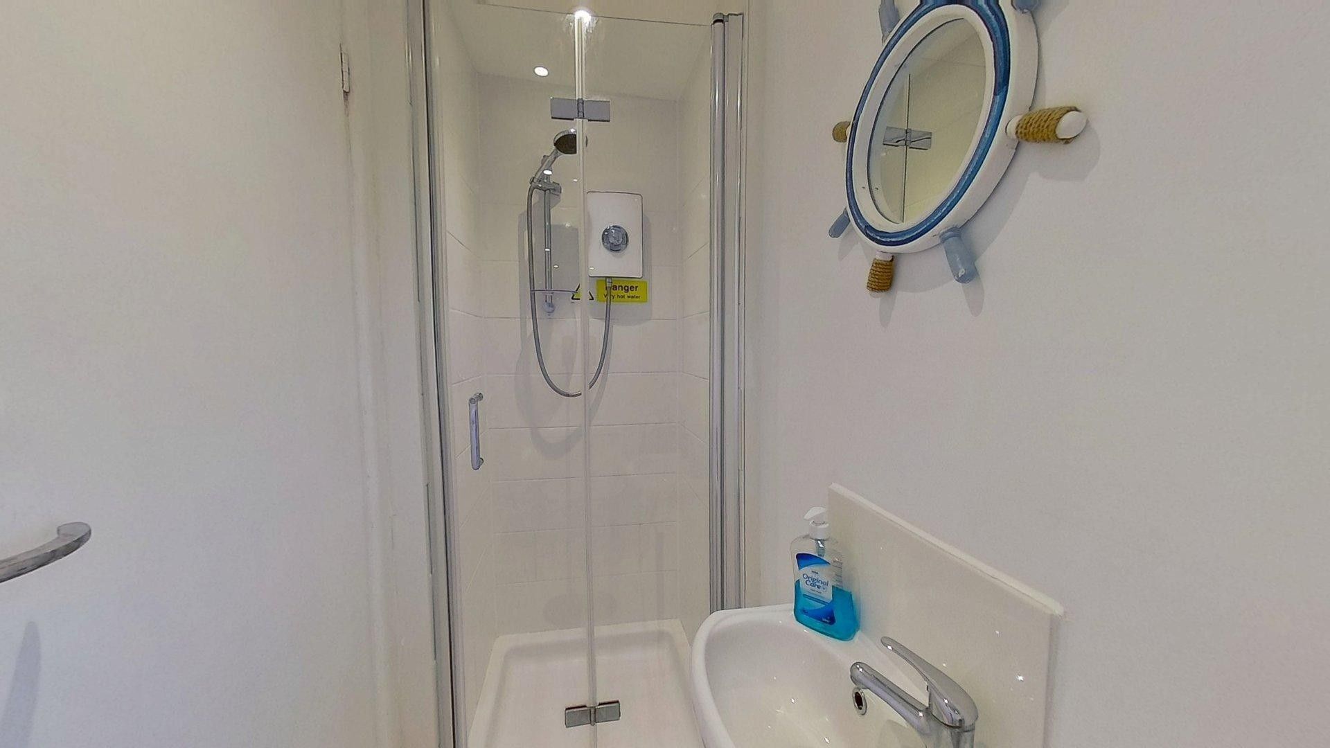 Une salle de bain avec une douche à parois de verre, un lavabo avec un miroir et un flacon de savon liquide.