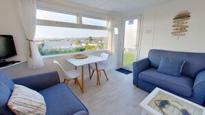 A modern living room with a blue sofa, a white table, and a TV. - E42 Vista Marina, Riviere Towans (Hayle)