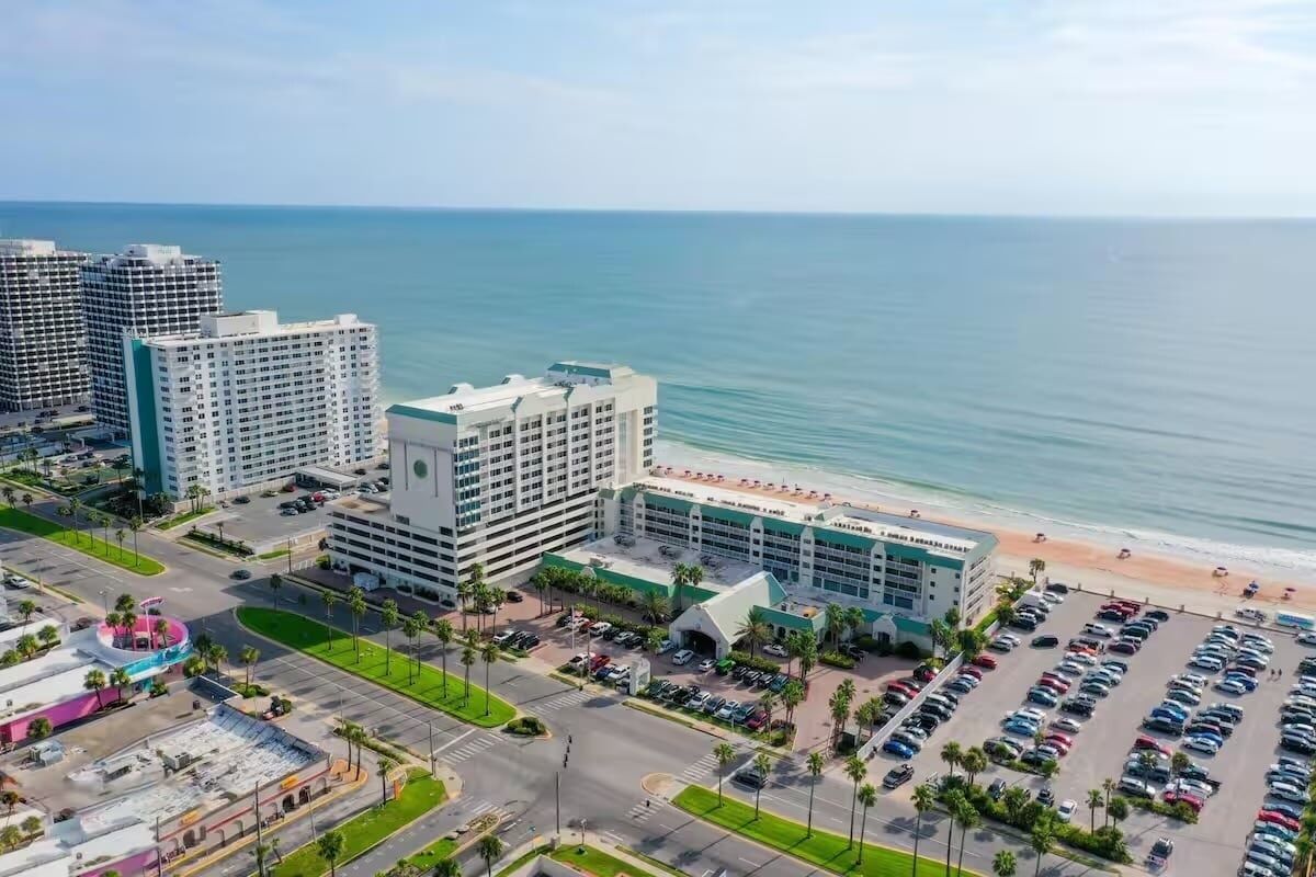 A hotel with a beachfront view, multiple parking lots, and a central building with a distinctive roof.