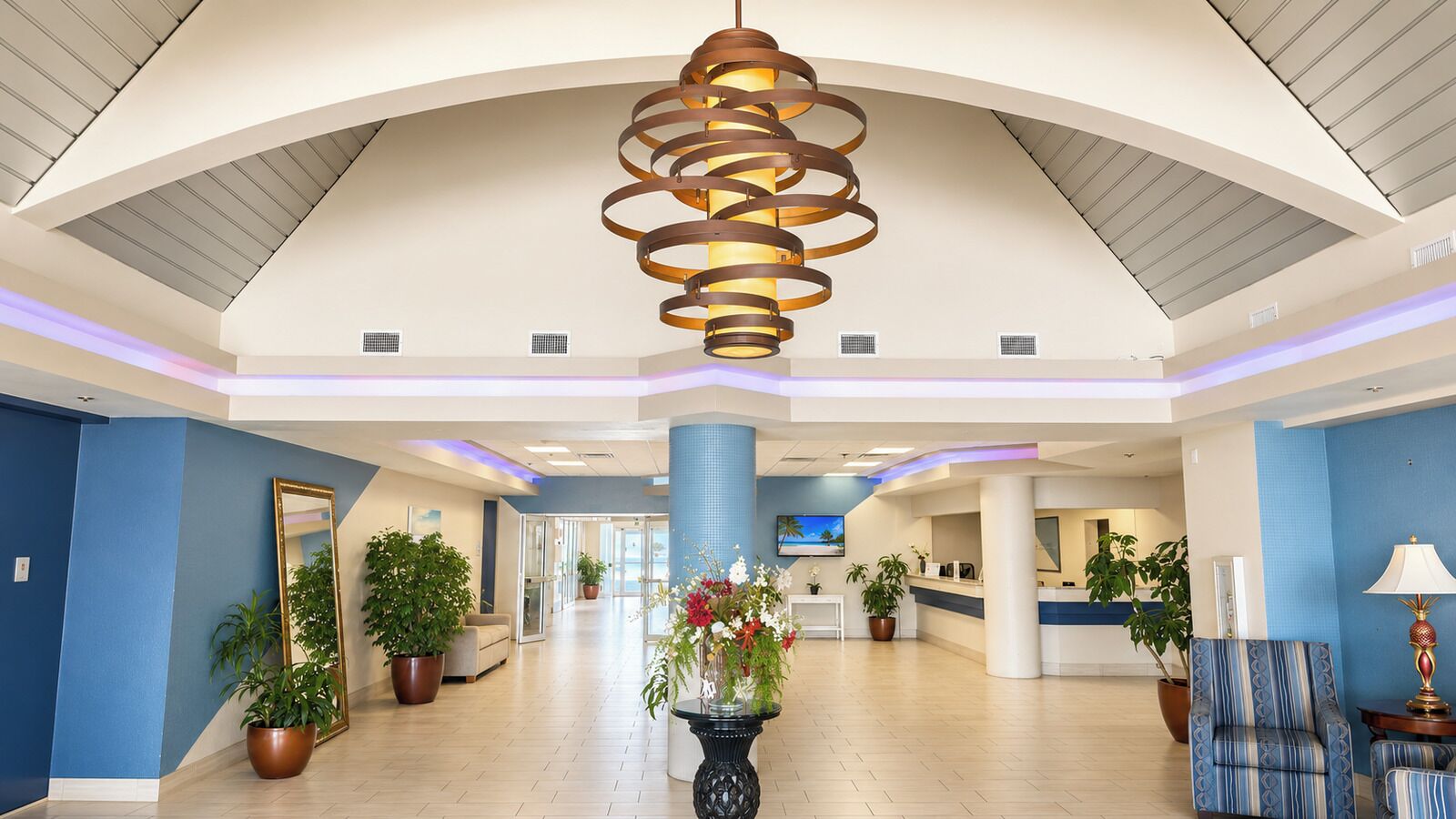 A spacious lobby with a high ceiling, a central chandelier, and multiple potted plants.