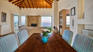 Un soggiorno spazioso con soffitto in legno, camino in pietra e ampia finestra vista mare.