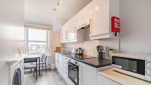 A modern kitchen with white cabinets, a built-in oven, a microwave, and a window overlooking a cityscape. - Sea View Penthouse - Walkable to Beach & Town (Norfolk)