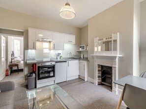 A modern kitchen with white cabinetry, a glass dining table, and a fireplace. - Apartment 4 - Beverley House (Norfolk)