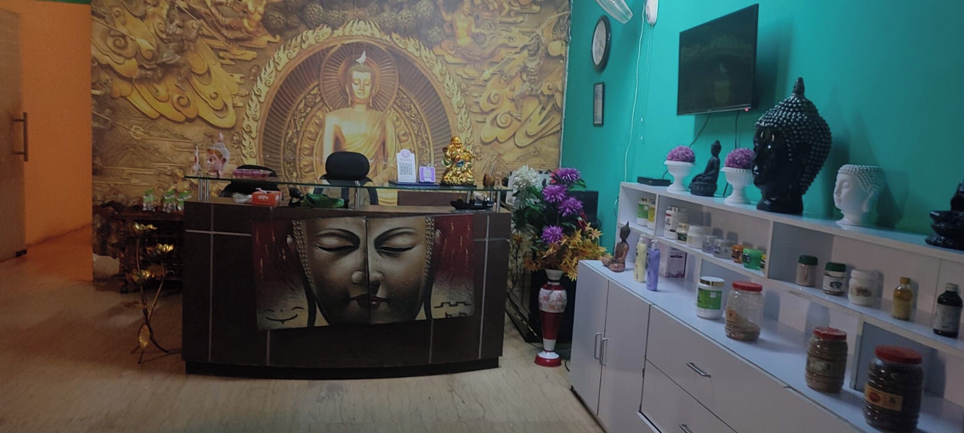 A reception area with a Buddha mural, a TV, and a shelf with various items.