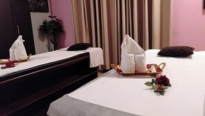 A hotel room with two beds, each with a white bedspread, pillows, and a tray with a folded towel and a rose. - The Hotel Am Bliss (Gurugram)
