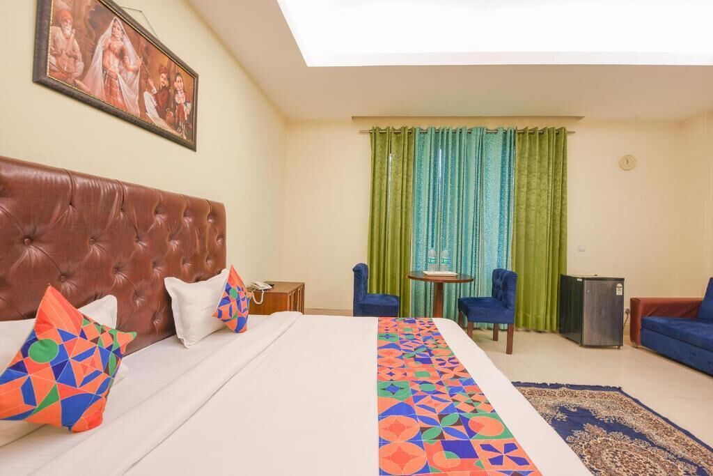 A hotel room with a large bed, a brown headboard, a small table with a chair, a blue sofa, and a green curtain.