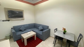 Una sala de estar moderna con un sofá seccional gris, una pequeña mesa de centro blanca, una mesa de comedor con sillas y una alfombra roja.