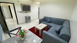 A modern living room with a grey sofa, a small table, a TV mounted on the wall, and a grey cabinet. - Rahet Al-Kharj Serviced Apartments (Al Kharj)