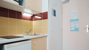 A compact kitchen with a sink, a small refrigerator, and a door with a notice. - Charming studio apartment for 2 people (Agde)