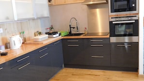 A modern kitchen with wooden cabinets, a stainless steel range hood, a built-in oven, and a wooden countertop.