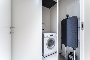 A compact laundry area with a front-loading washing machine and a drying rack. - Unique Luxury and Quiet in Porto's Best Location (Porto)